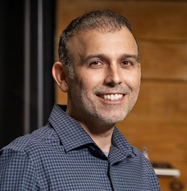 A man in a blue plaid shirt is smiling for the camera.