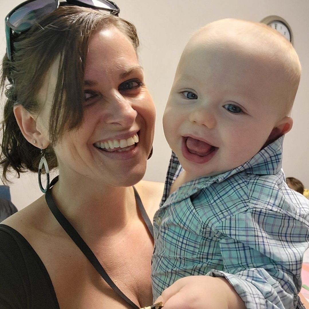 A woman is smiling while holding a baby in her arms