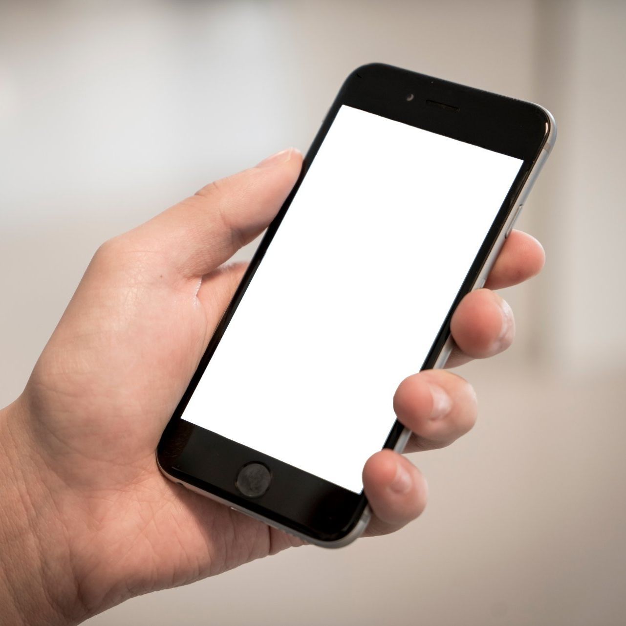 A hand is holding a cell phone with a white screen
