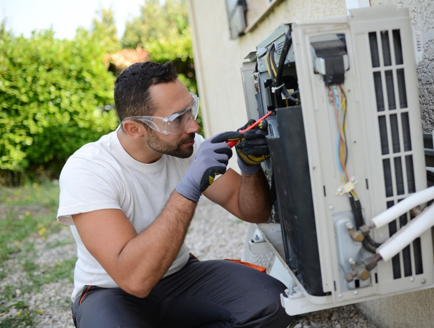 Technician repairing an air conditioning unit outdoors, wearing safety glasses and gloves. — Cooling Plus Refrigeration & Airconditioning in Ciccone, NT