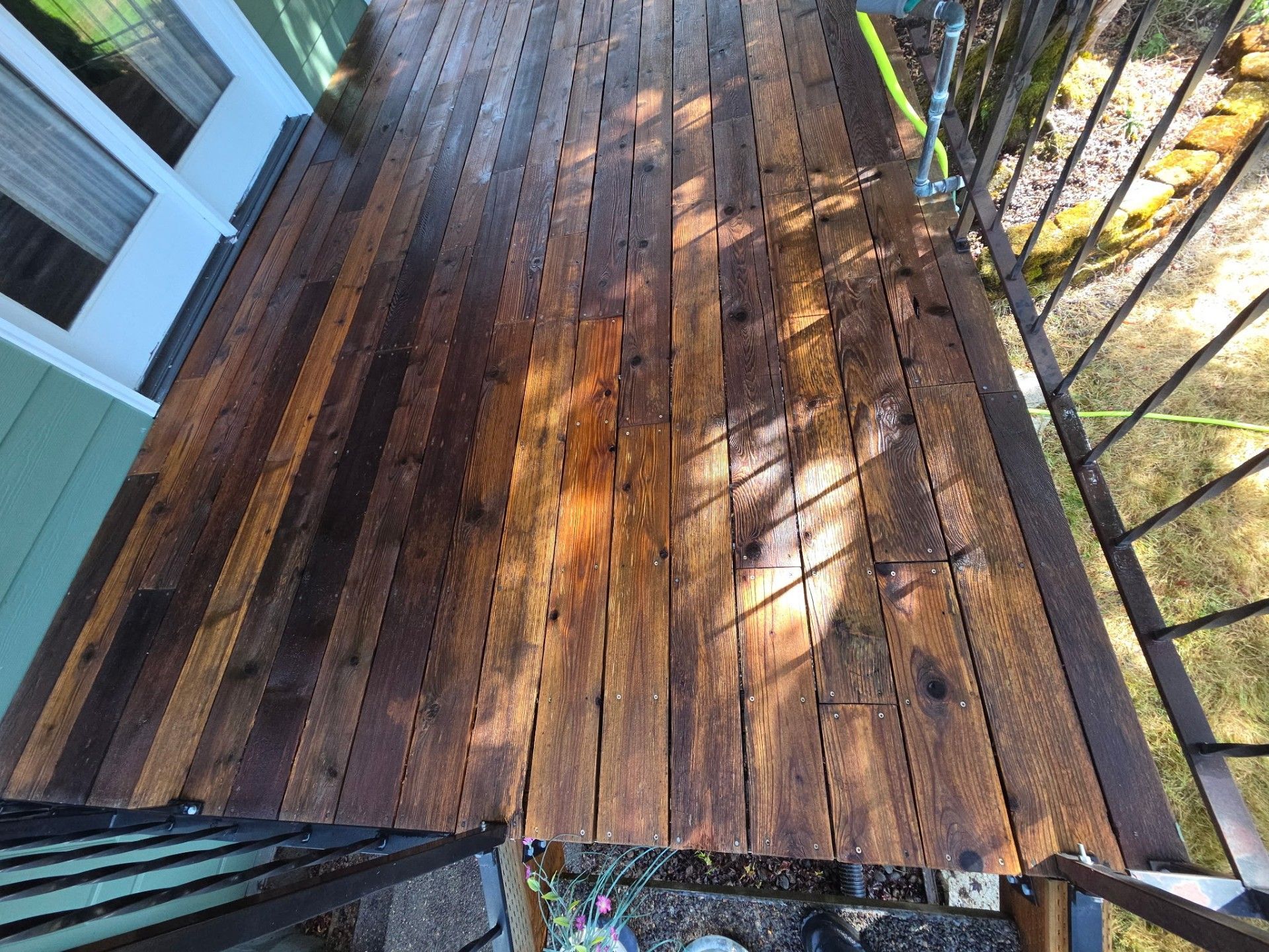 Sunlit wooden deck with metal railing and outdoor staircase viewed from above