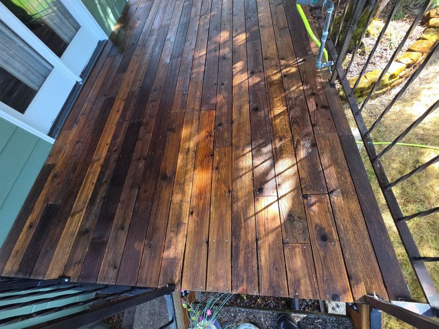 Sunlit wooden deck with metal railing and outdoor staircase viewed from above