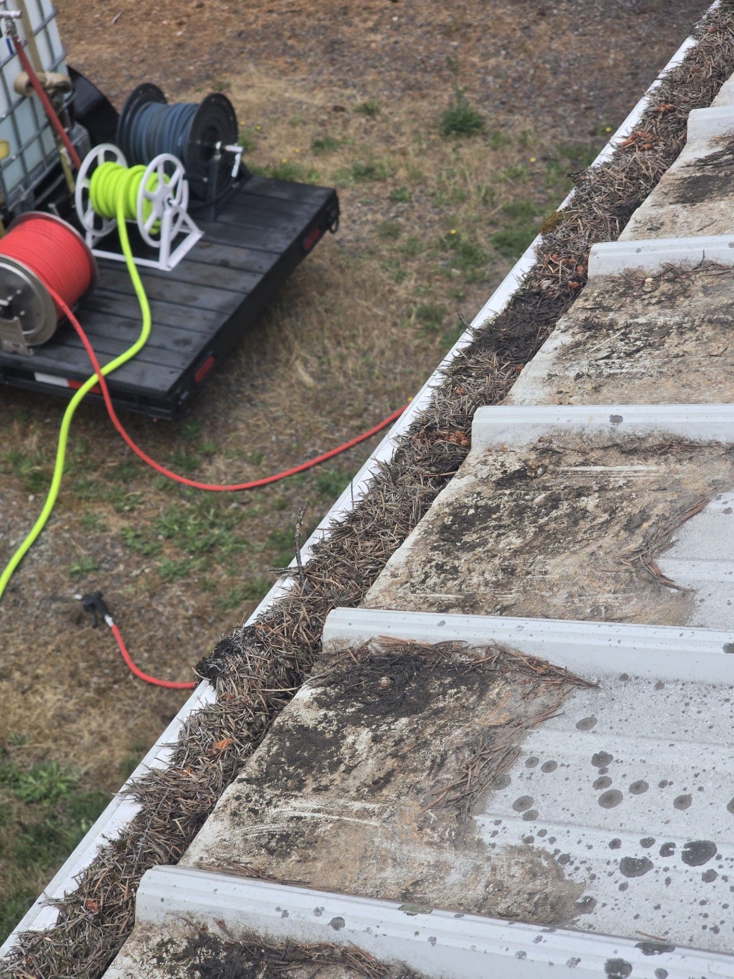 Construction area with red and neon green hoses on a cart beside a concrete curb and gravel trench.