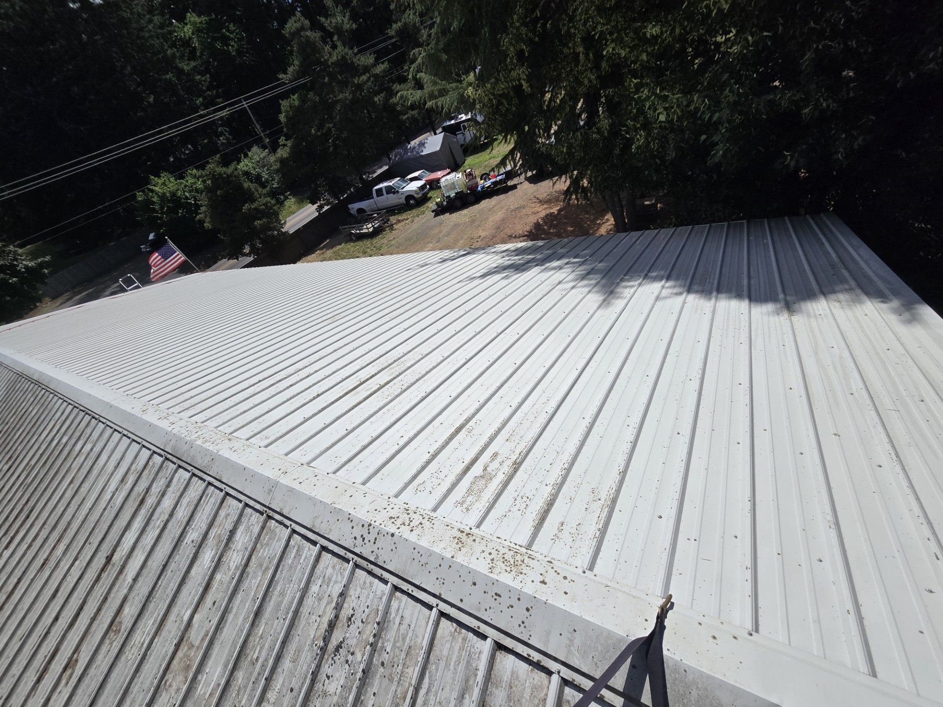 White corrugated metal roof on a wooded hillside with cars and utility lines in the background