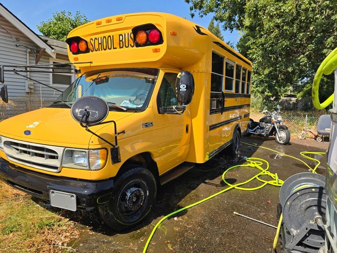Yellow school bus parked in a driveway with hoses and tools around it