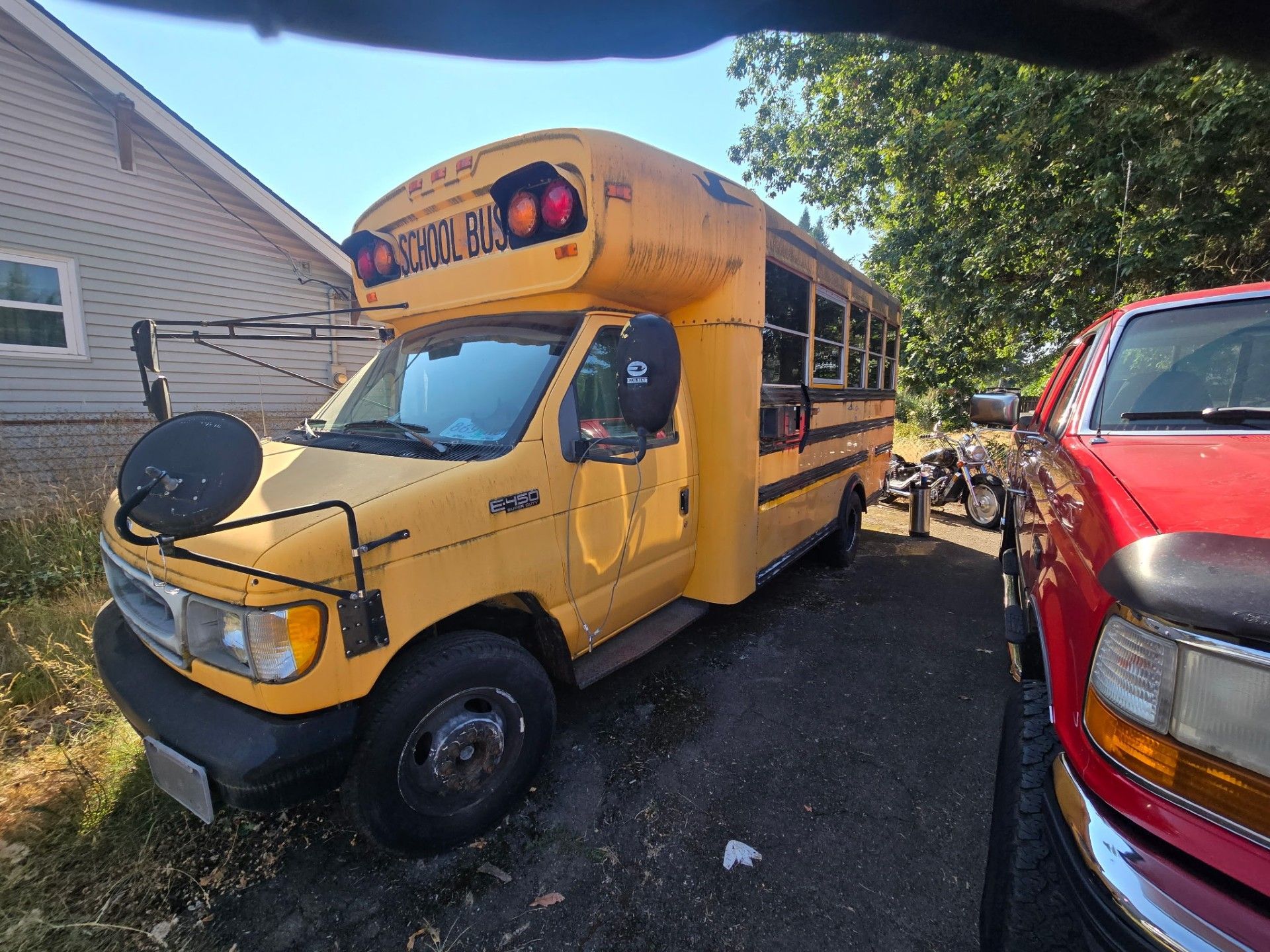 Yellow school bus parked between houses and a red vehicle in a driveway