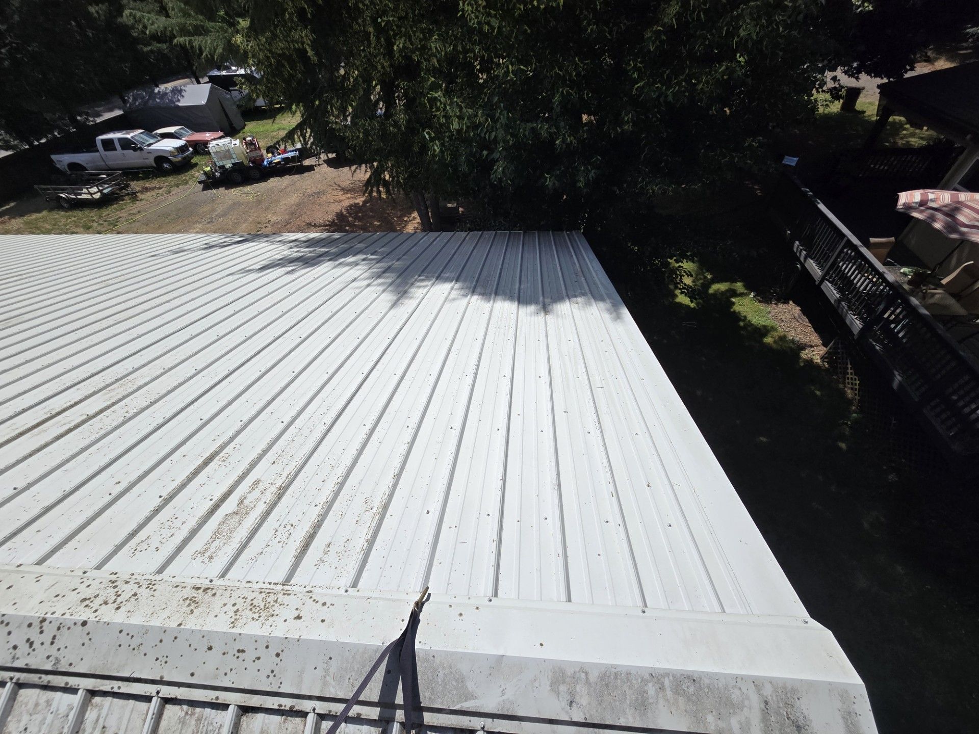 White corrugated metal roof viewed from above, with trees and parked cars in the background