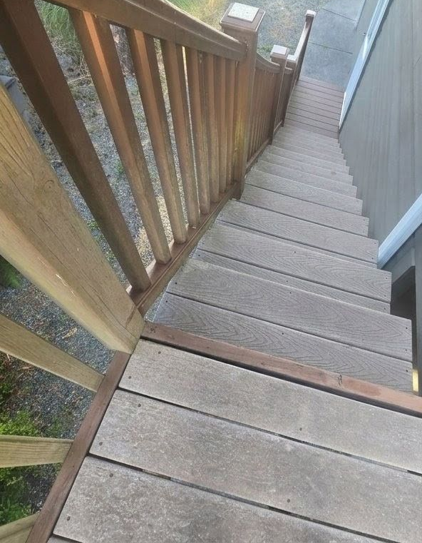 Steep wooden outdoor staircase with railing, viewed from the top looking down.