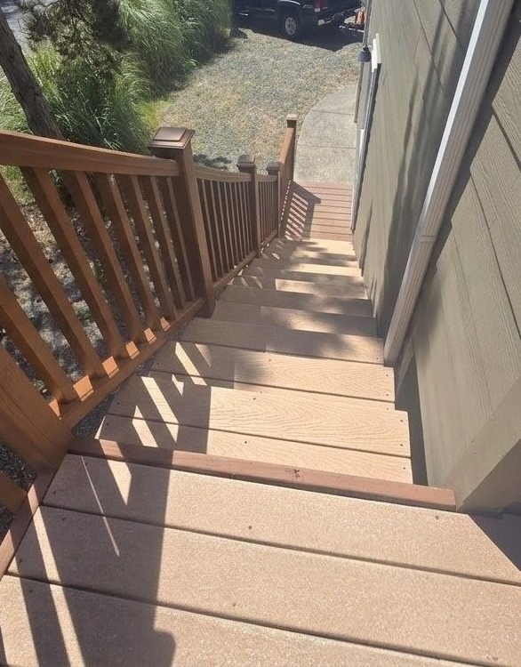Steep outdoor wooden staircase with railings, leading down beside a house to a yard.