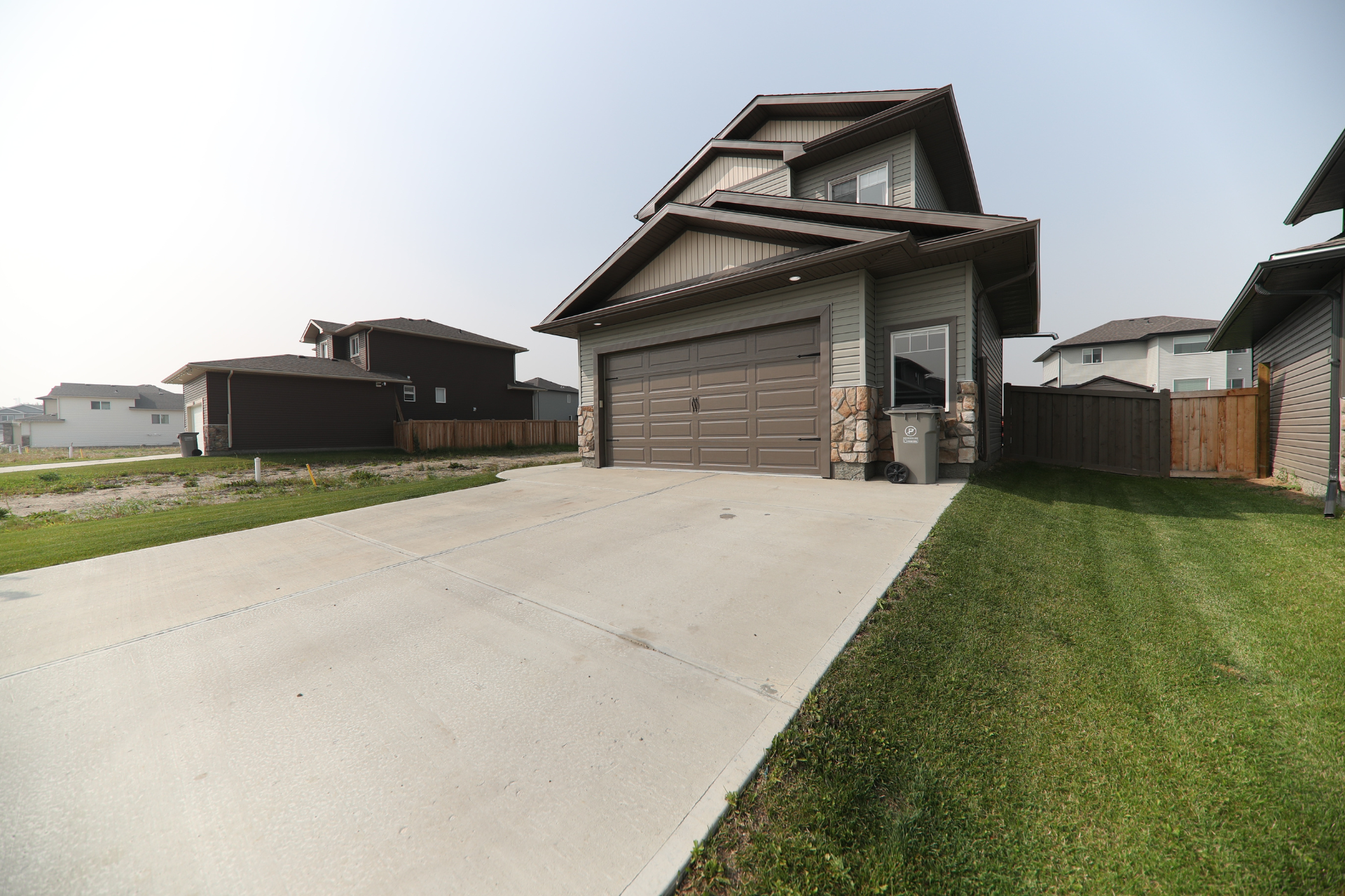 Modern two-story house with a steep roof, garage, and wide concrete driveway in a suburban neighborhood