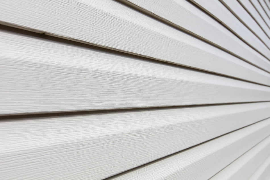 Close-up of white horizontal siding panels with thin dark gaps, viewed at an angle