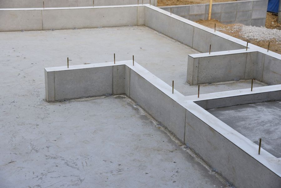 Concrete foundation of a building under construction, featuring walls and a floor. Rebar is visible.