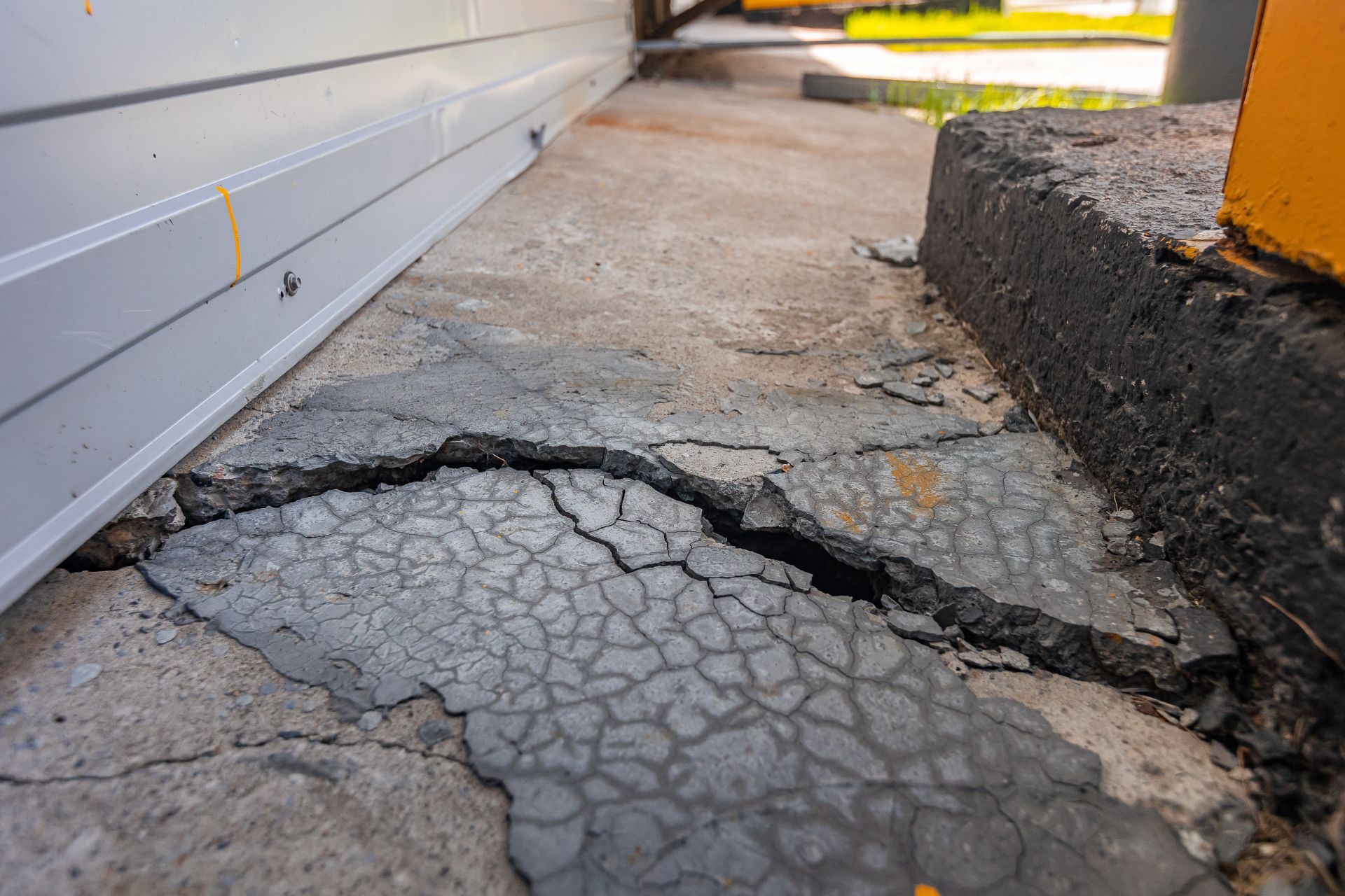 Cracked concrete pavement beside a building. The cracks are deep.