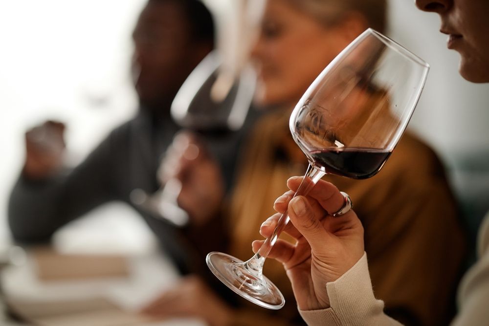 Hand holding a wine glass with red wine at a blurred tasting event