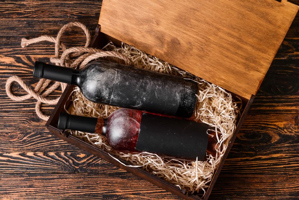 Two wine bottles in a wooden crate with straw on a rustic table