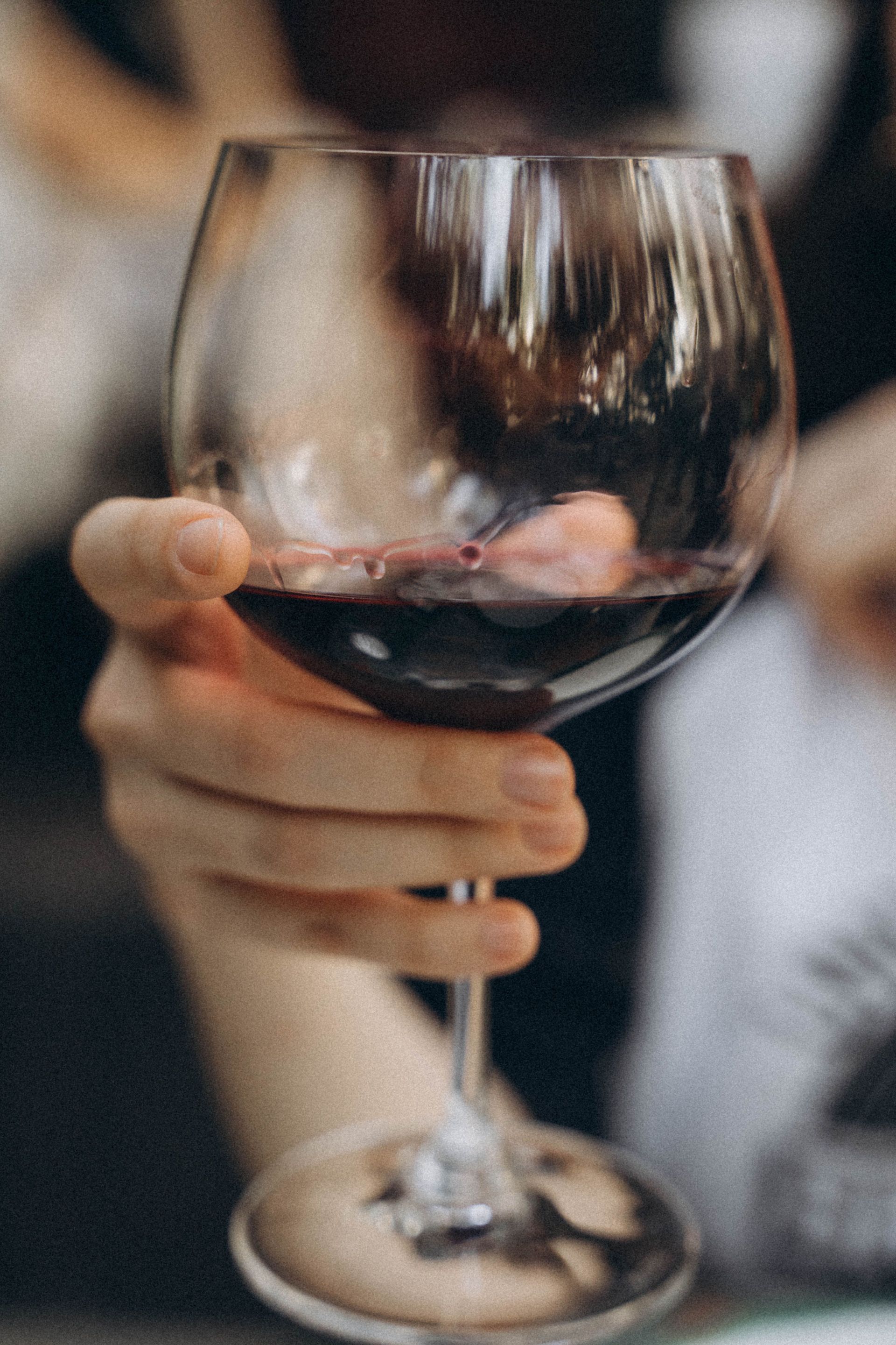 Hand holding a glass of red wine in a softly lit setting