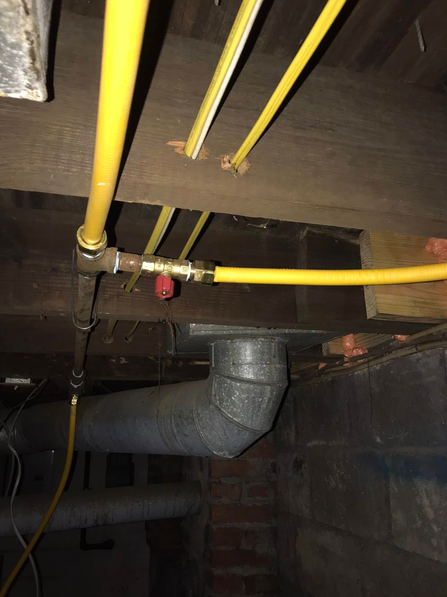 Yellow gas pipes and a valve are installed beneath a wooden ceiling. A black vent pipe is also visible.