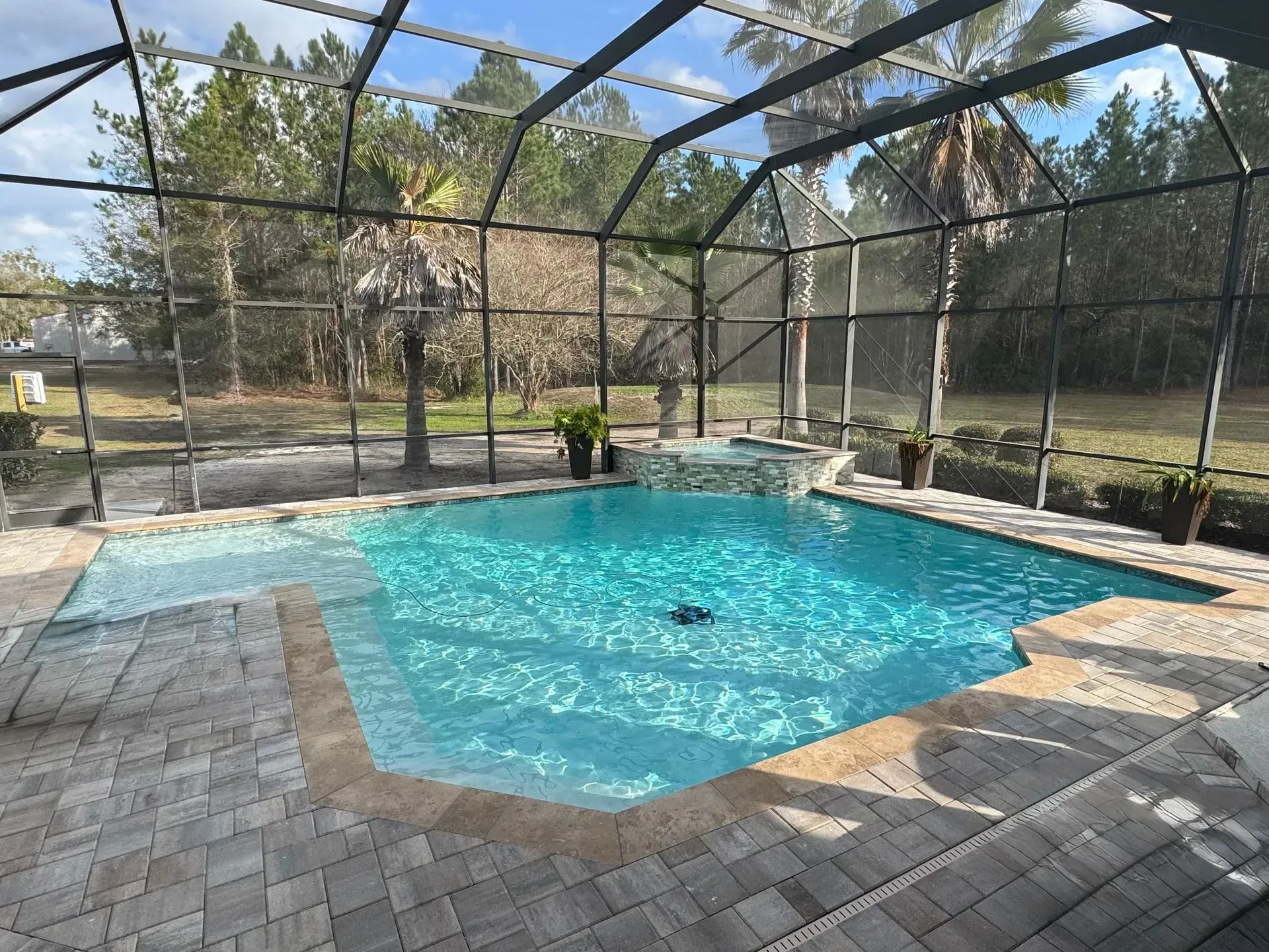 Screened-in backyard pool with turquoise water, paver deck, and lounge chairs in bright daylight
