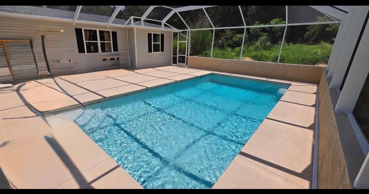 Screened backyard pool with blue water, beige deck, and a house patio in the background