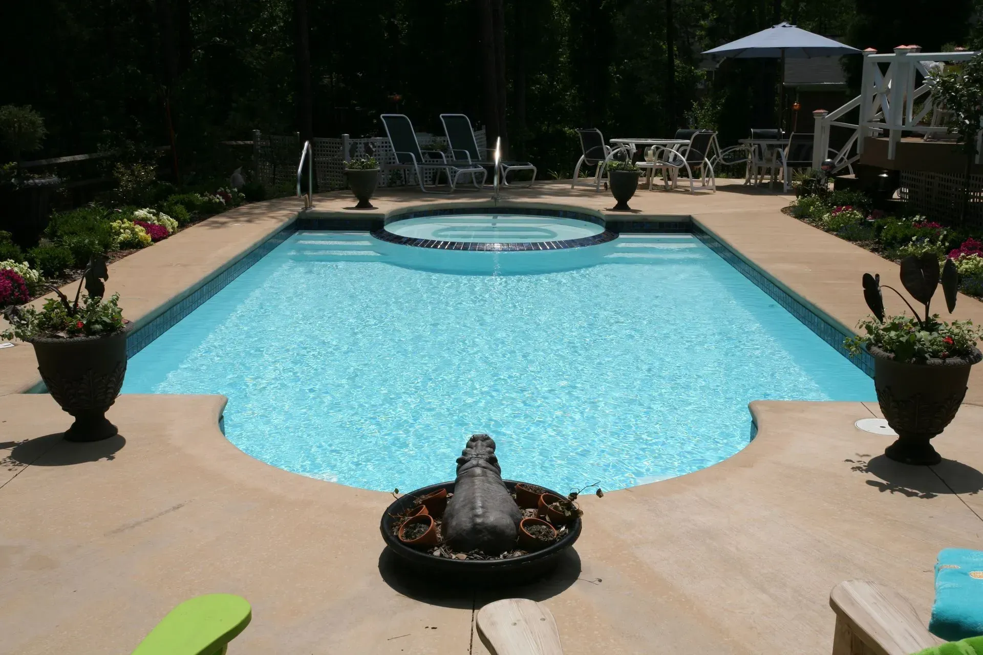 Backyard pool with a circular hot tub, potted plants, and lounge chairs in bright sunlight