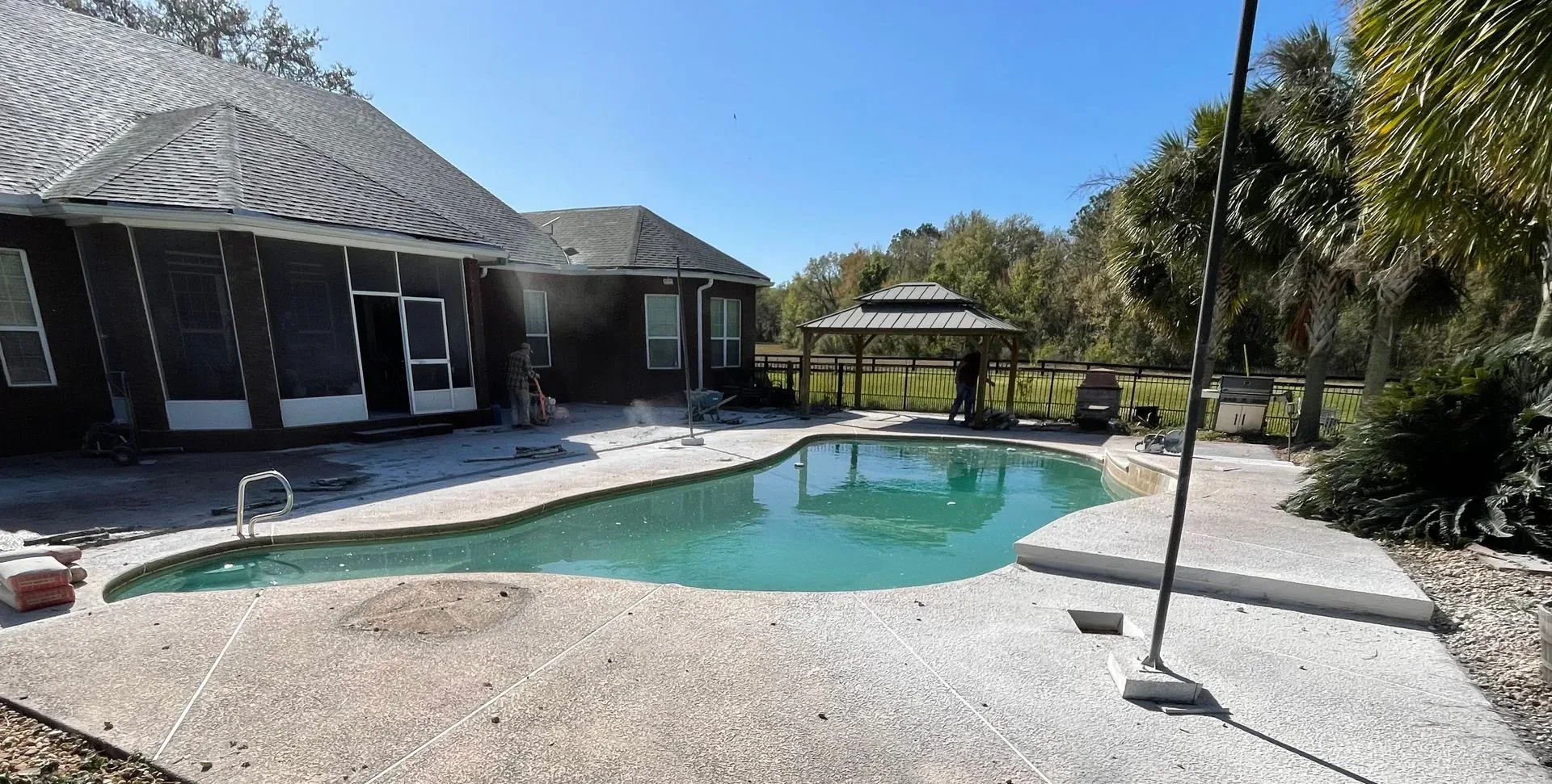 Backyard patio with a swimming pool, lounge chairs, and palm trees beside a house