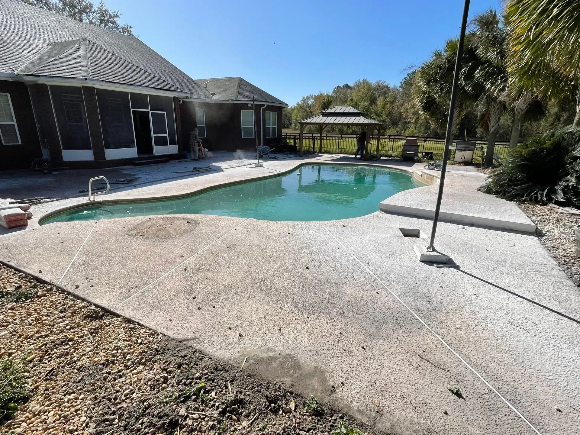 Backyard pool with a concrete patio, lounge chairs, and a house in bright sunlight