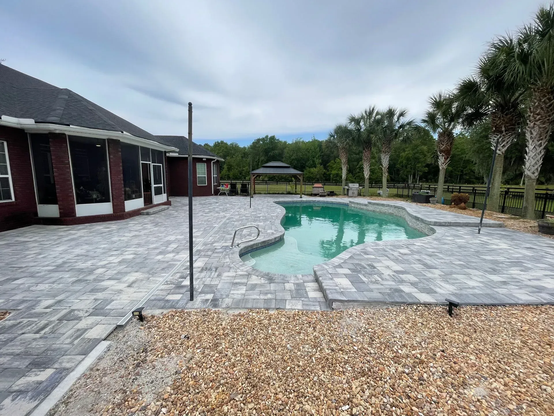 Backyard with a turquoise pool, paved patio, and palm trees beside a house