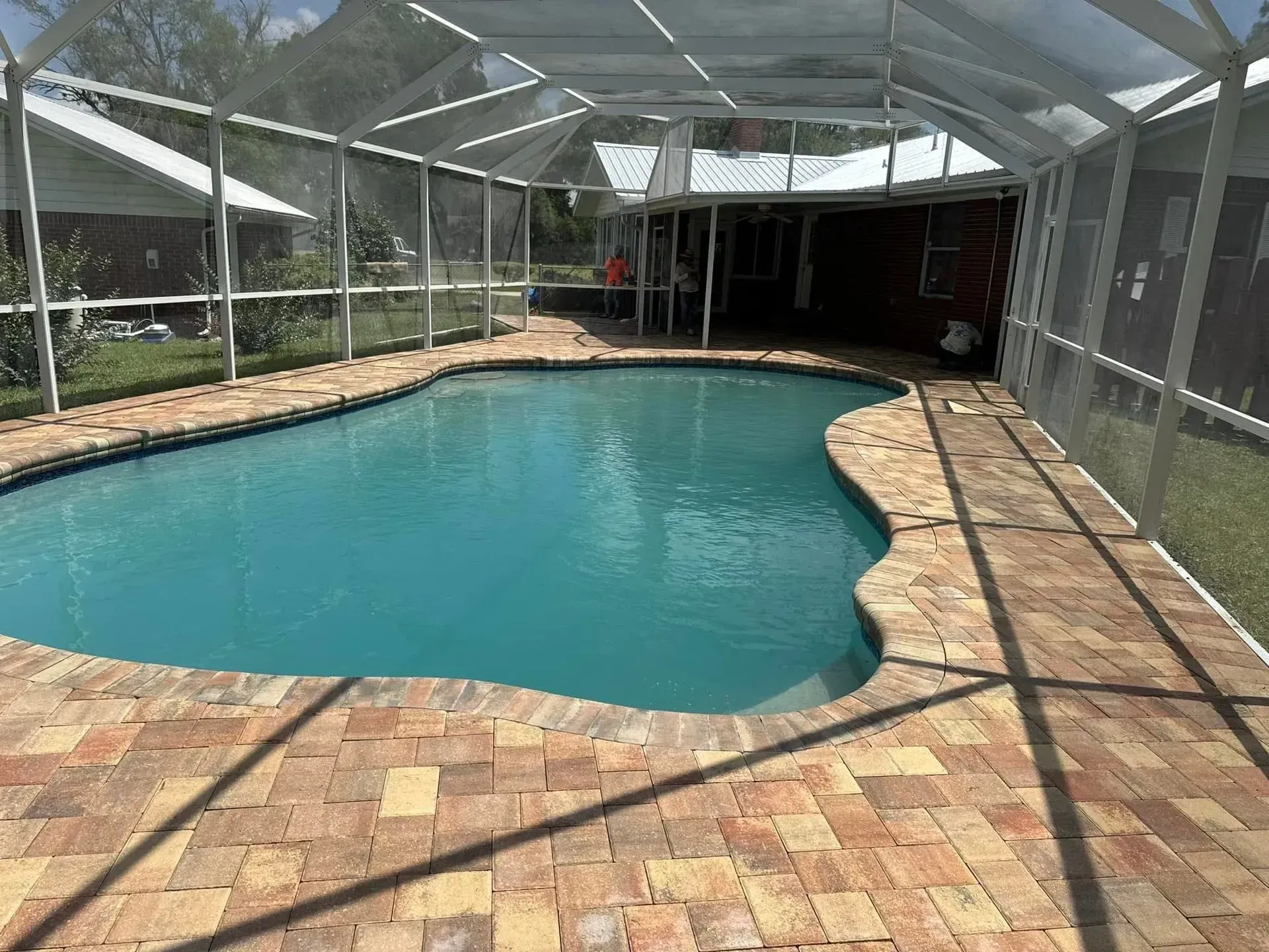 Screened-in backyard pool with blue water and tan brick patio, covered by a white enclosure.