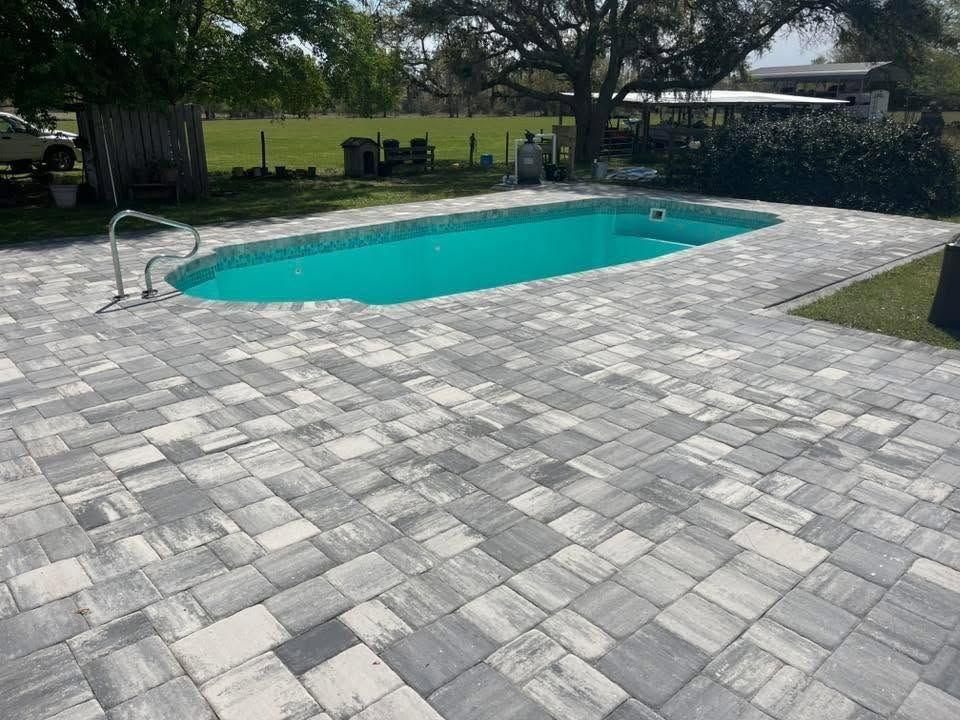 Backyard swimming pool with gray stone patio and a green lawn in the background