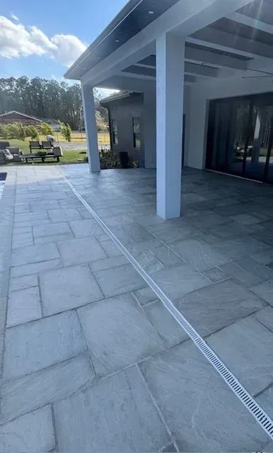 Covered outdoor patio with gray stone tiles, white columns, and a view of the yard beyond.