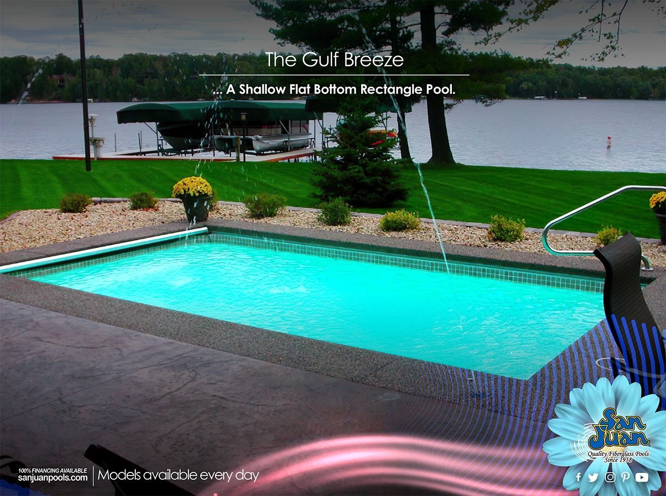 Rectangular turquoise backyard pool beside a patio, with lawn and lake in the background