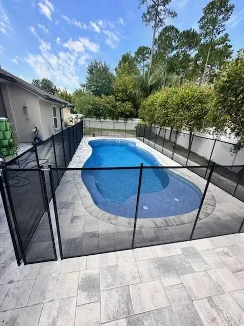 Backyard pool enclosed by black safety fence beside a house and patio tiles