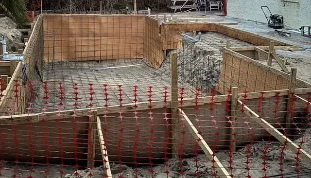 Construction site with a rebar foundation pit and wooden formwork being built.