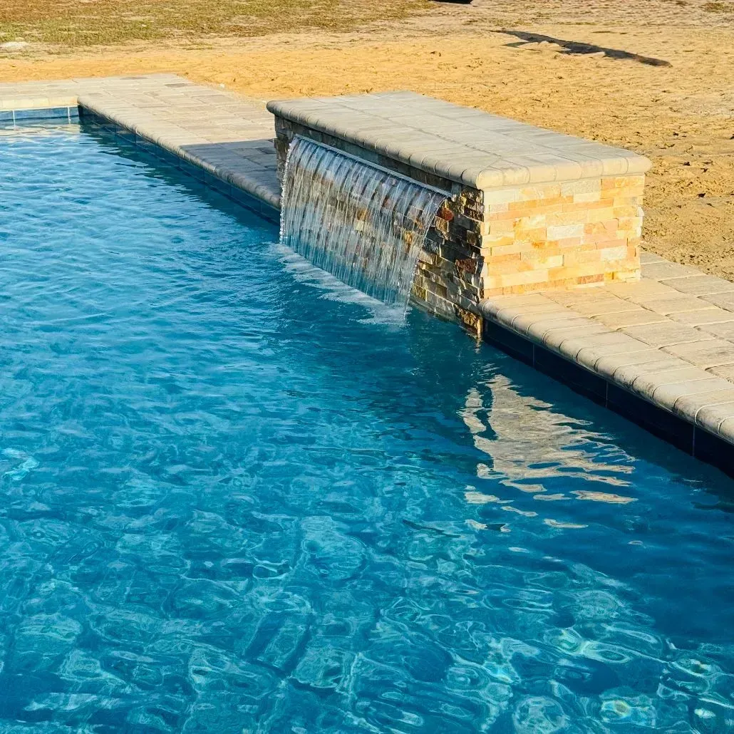 Blue swimming pool with a small stone waterfall spillway at the edge