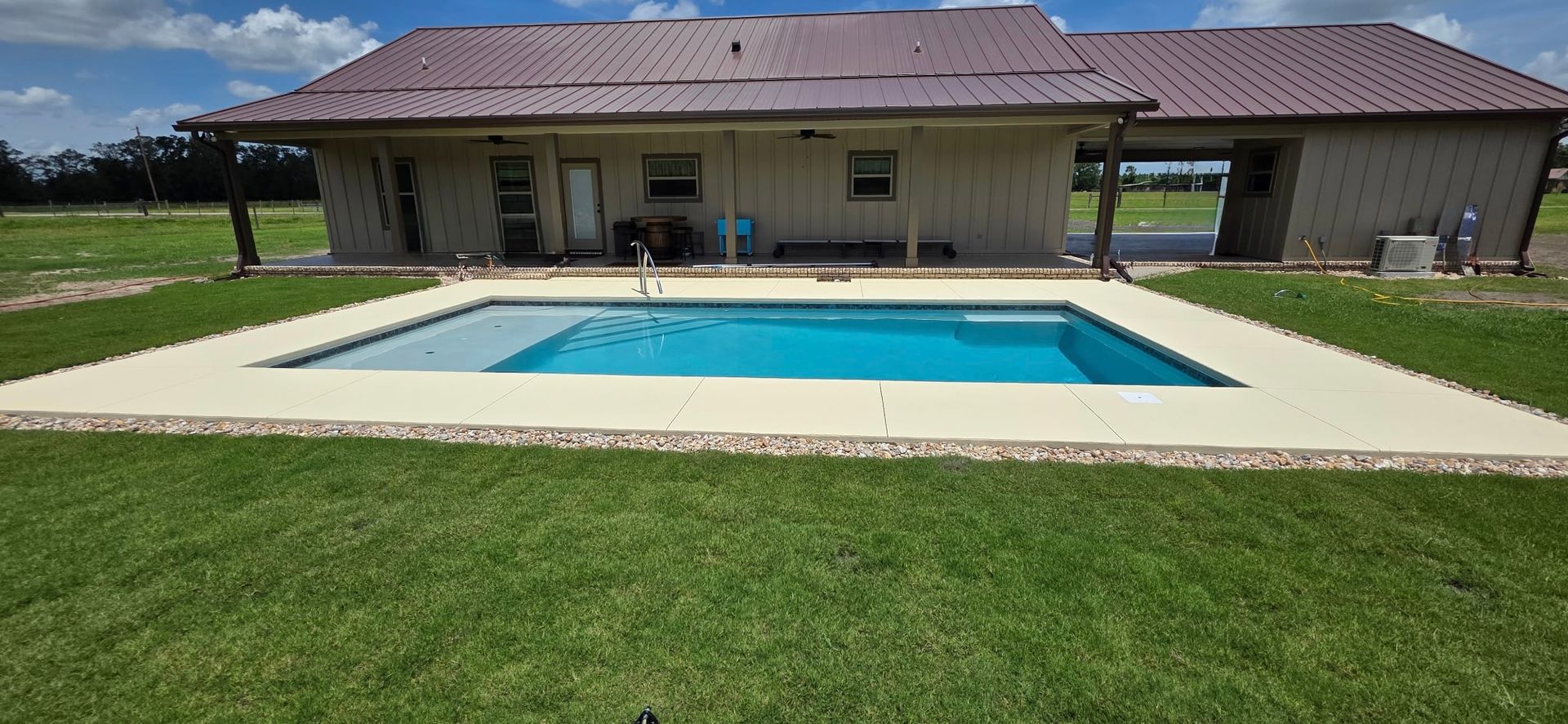 Backyard pool in front of a single-story house with a red roof and green lawn