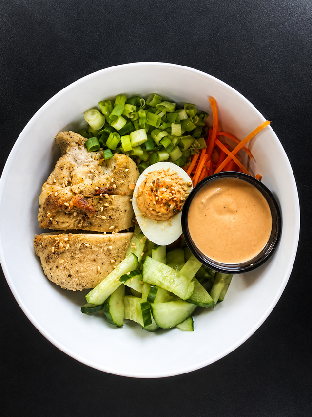 Donburi bowl with pork, cukes, carrots, miso deviled egg, green onion, and bang bang sauce over sticky rice