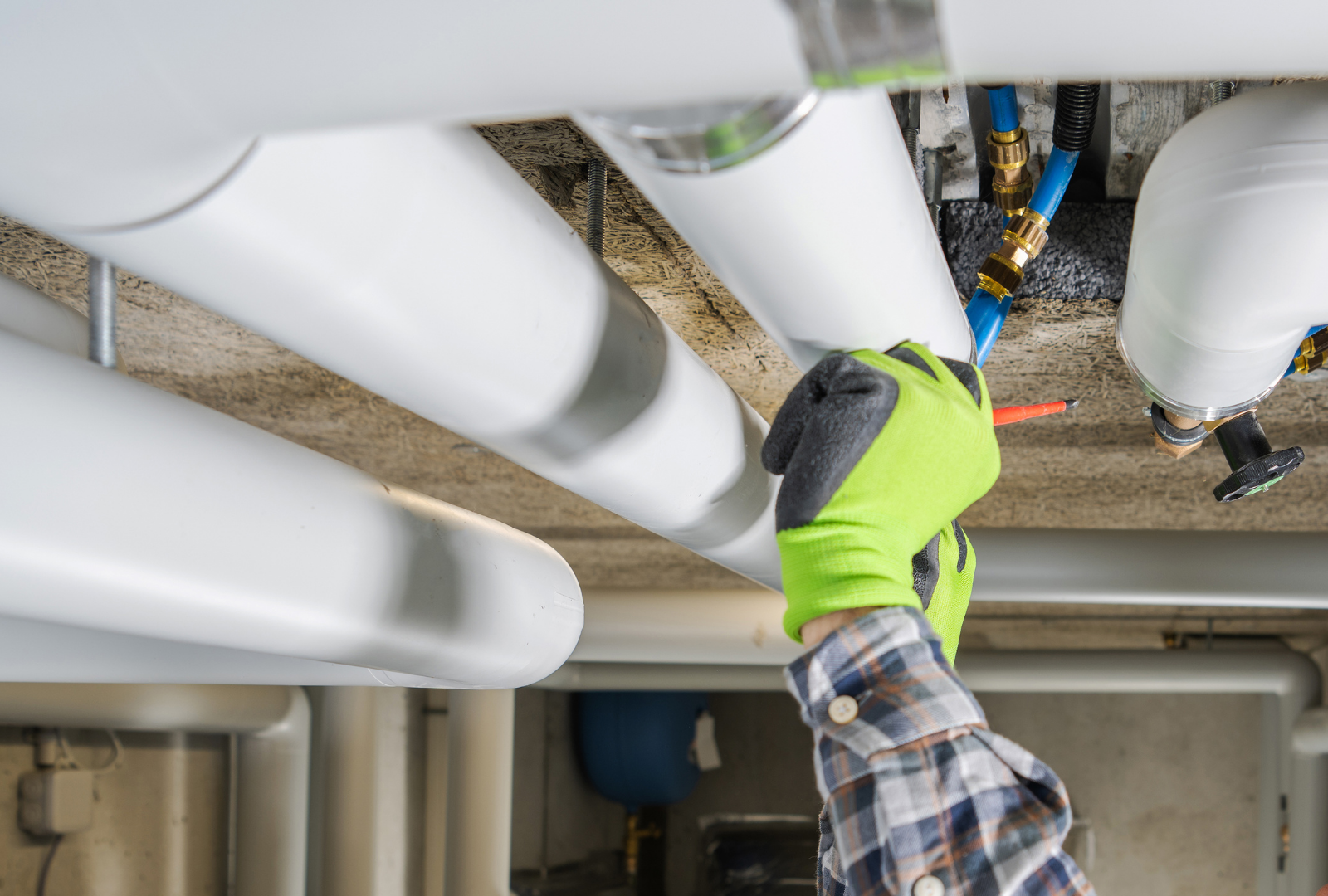 Gloved technician adjusting pipes beneath insulation in a ceiling utility space