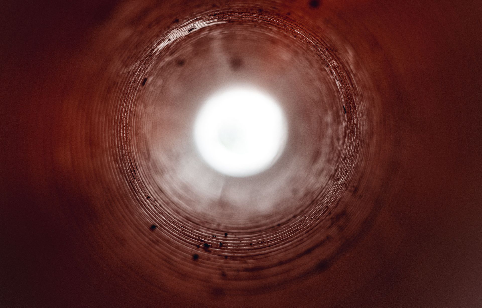 Inside a reddish cylindrical tunnel, a bright circular opening glows at the center.