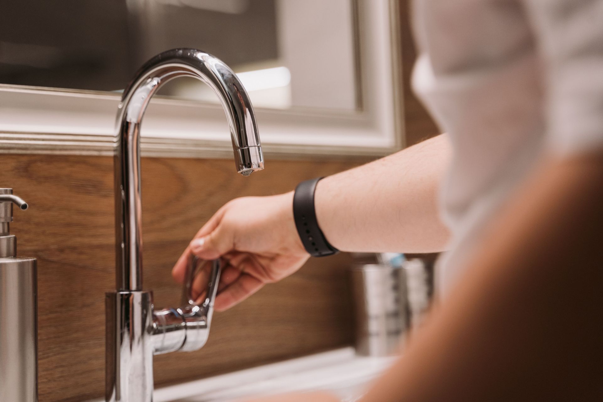 Hand turning on a kitchen faucet over a sink with wooden backsplash