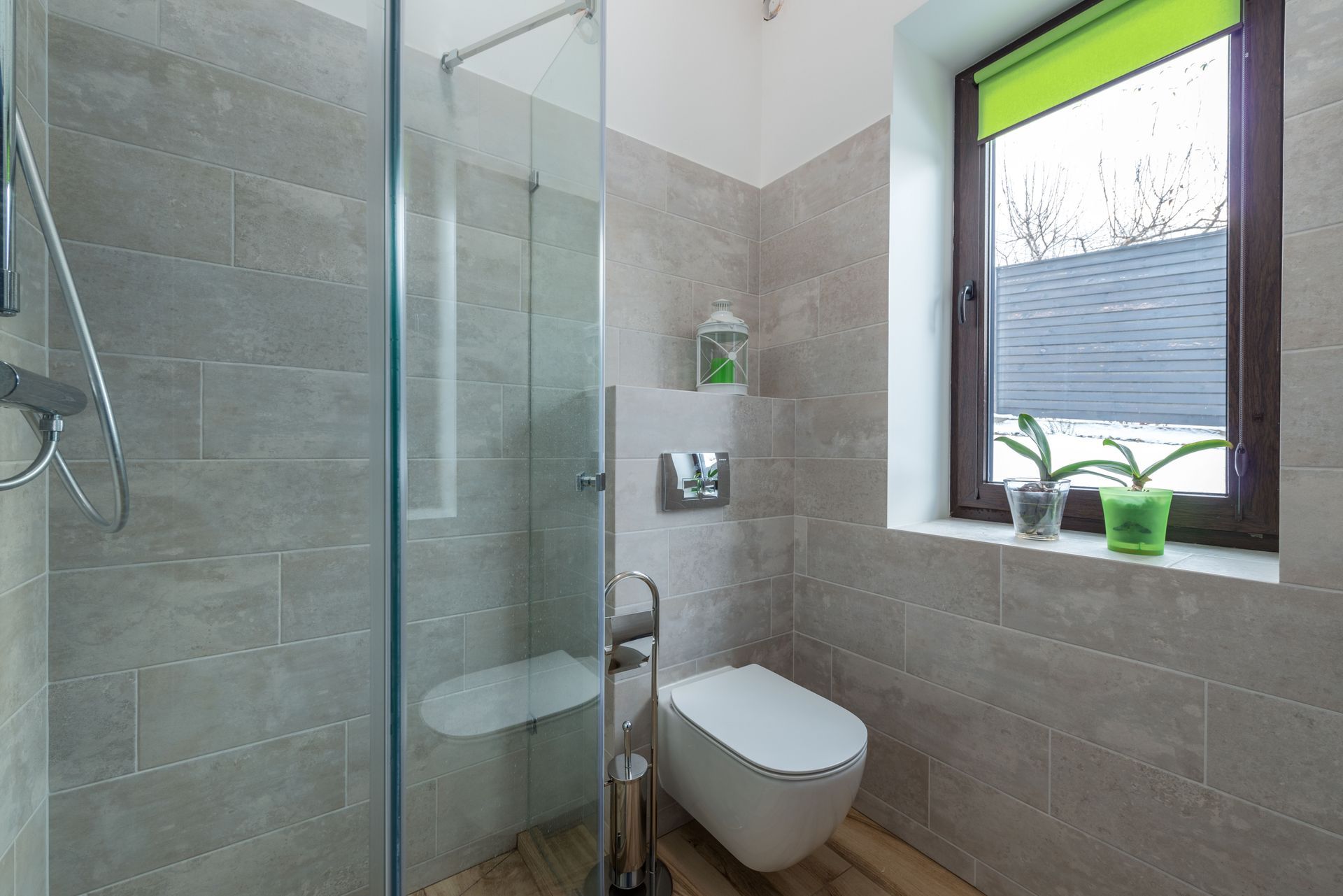 Modern bathroom with glass shower, wall-mounted toilet, and window with green plants.