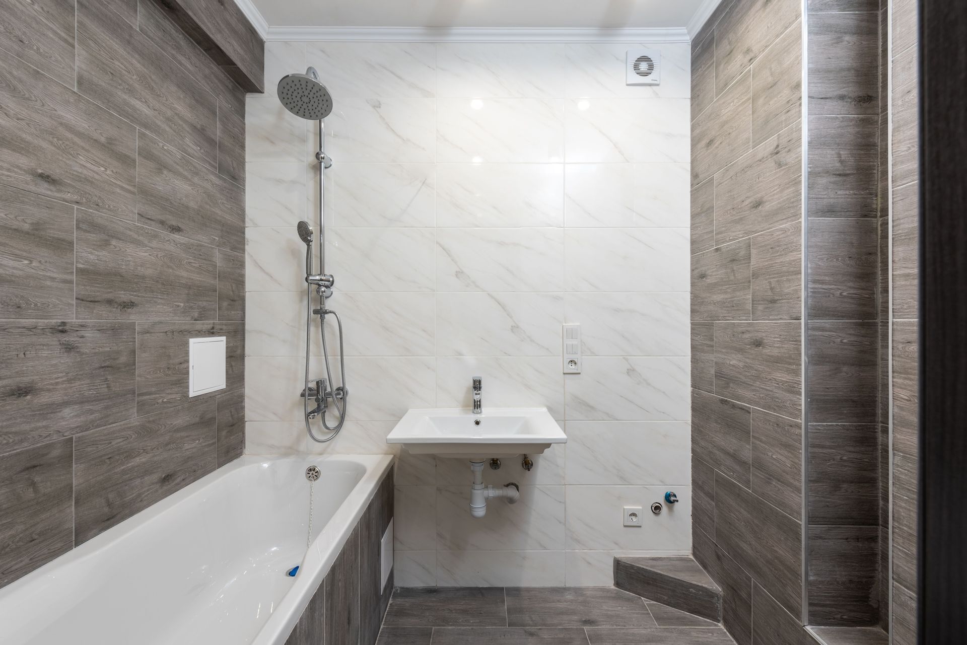 Modern bathroom with white tub, wall-mounted sink, and gray tile walls and floor