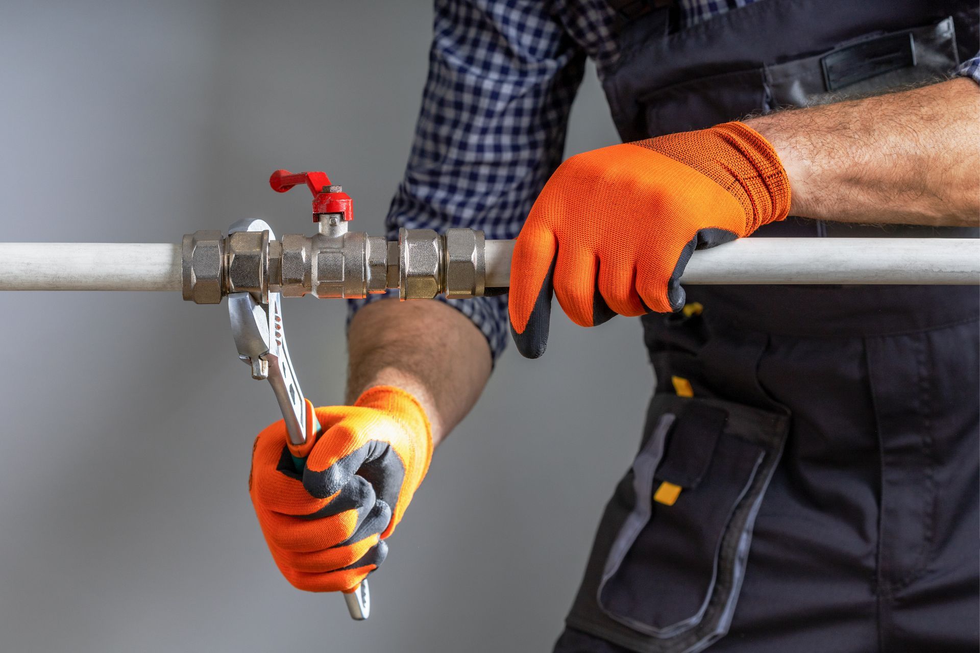 Gloved worker tightening a pipe valve with a wrench on a metal pipeline