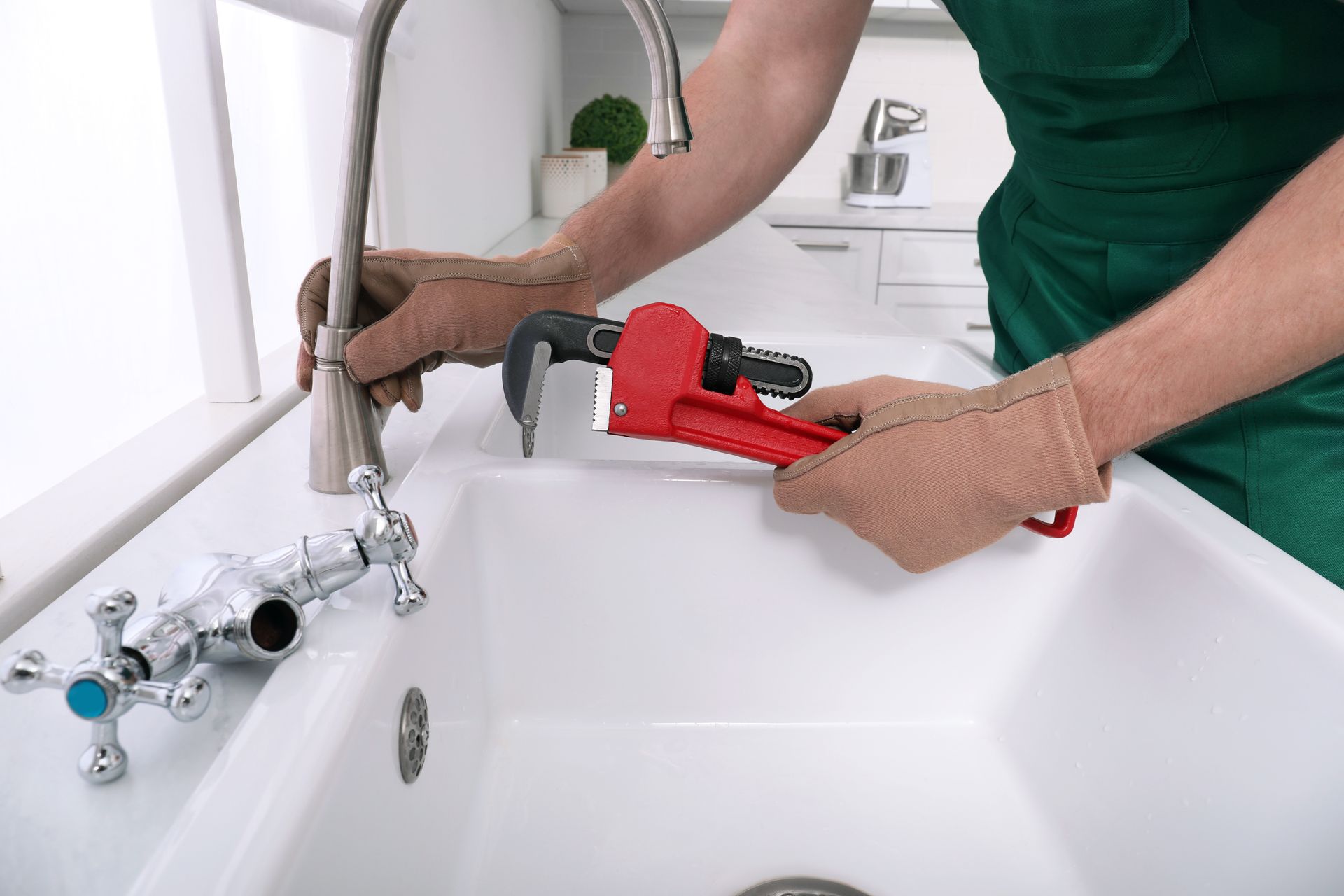 Plumber tightening a faucet with a red wrench beside a white sink