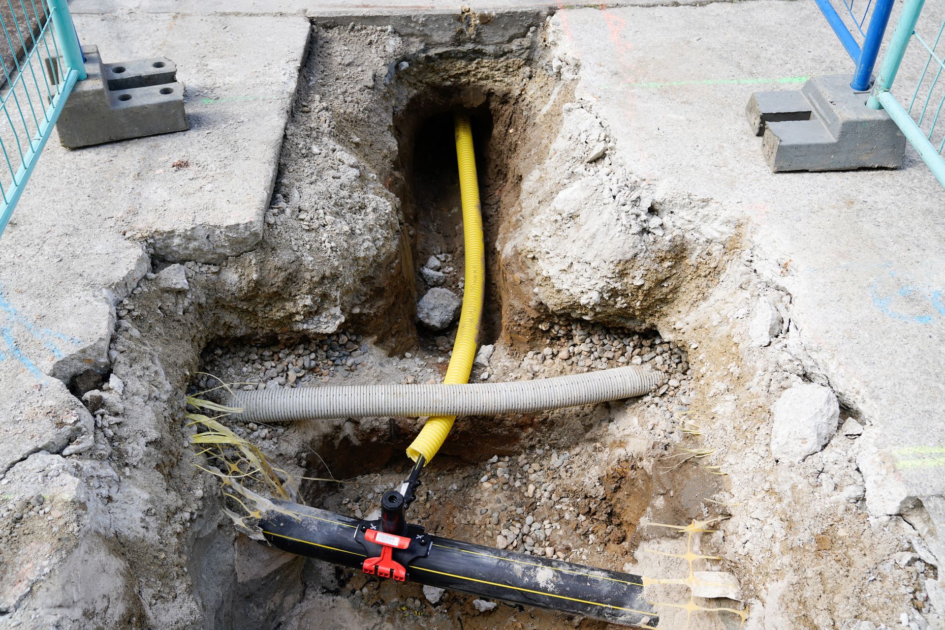 Concrete trench with exposed yellow cable, gray conduit, and a red valve under a damaged walkway