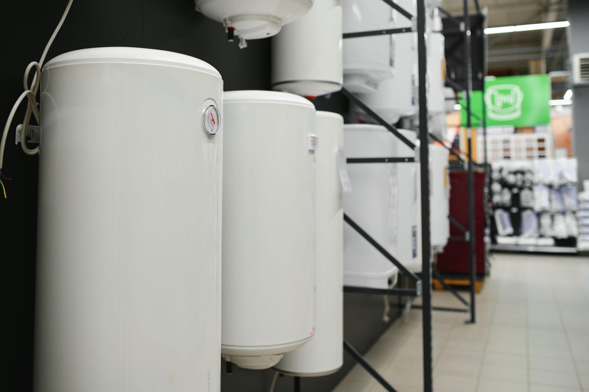 White water heaters lined up in a store aisle with shelving and lights in the background
