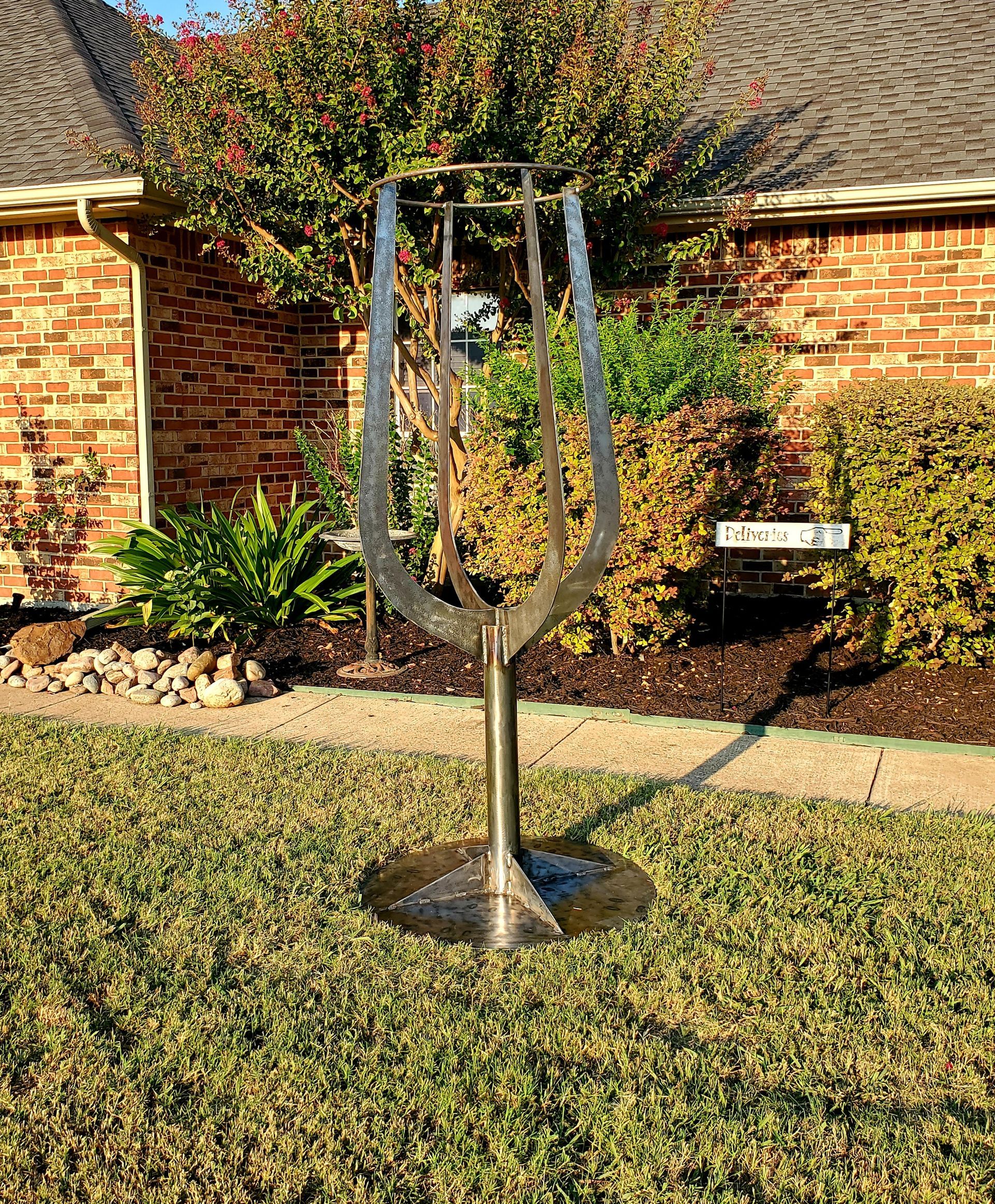 A sculpture of a wine glass is sitting in the grass in front of a brick house.