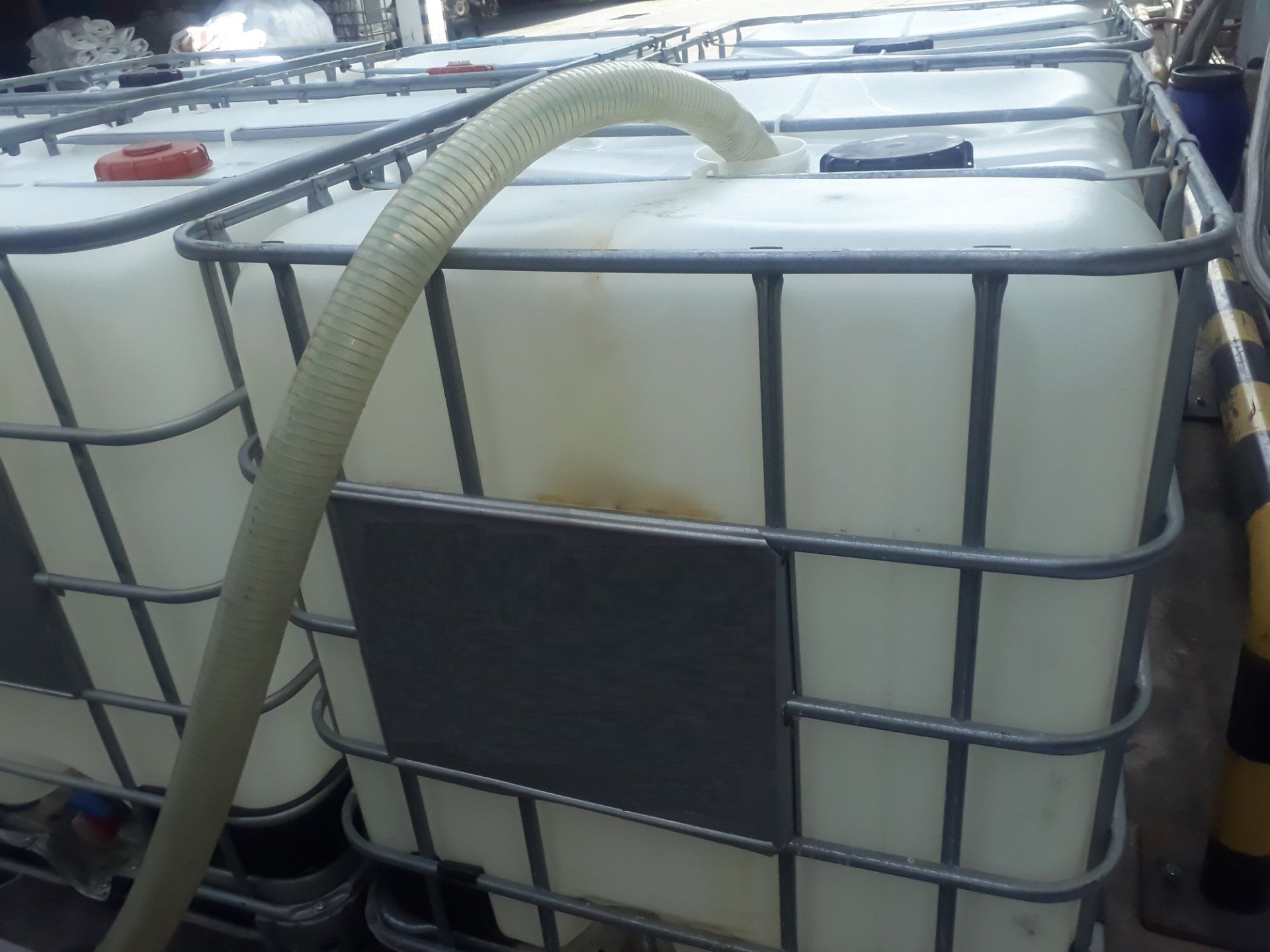 Contenitori IBC bianchi all'interno di gabbie metalliche, con tubo flessibile inserito.