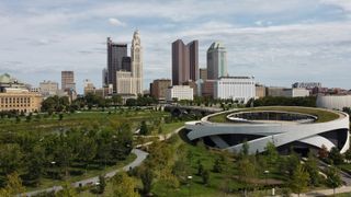City skyline above a lush park with a modern white ring-shaped building in the foreground