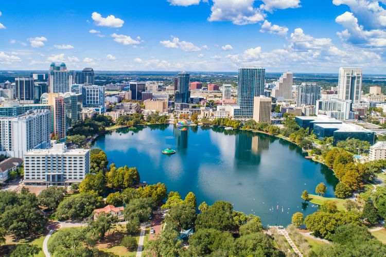 Aerial view of a city skyline around a large blue lake with green trees and buildings under a bright sky