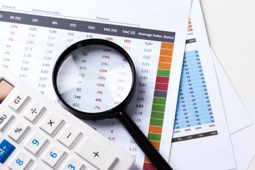 Magnifying glass over financial charts with calculator and spreadsheet on a desk